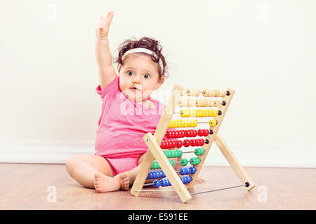 Baby Girl sitting on floor et levant la main avec un abaque à côté d'elle Banque D'Images