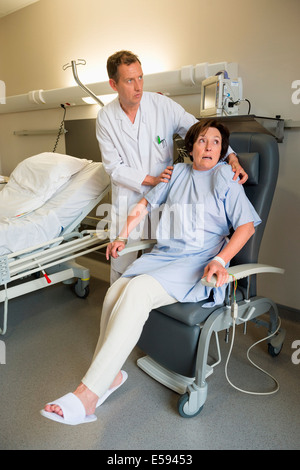 Médecin homme femme aidant à patient assis sur une chaise à l'hôpital Banque D'Images