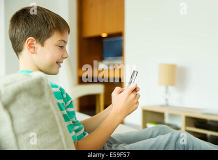 Boy using cell phone in living room Banque D'Images