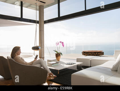 Woman using cell phone in modern living room Banque D'Images