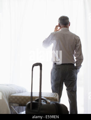 Businessman talking on cell phone in hotel room Banque D'Images