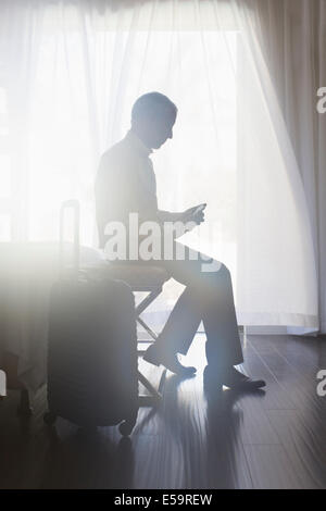 Businessman using cell phone in hotel room Banque D'Images