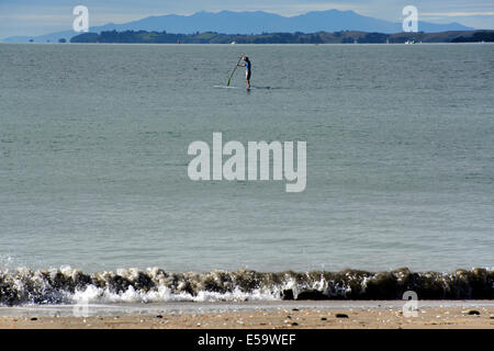 Man Stand Up Paddle Surf près de la plage de Takapuna avec la péninsule de Coromandel dans l'arrière-plan, Auckland, Nouvelle-Zélande Banque D'Images