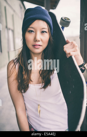 Korean woman carrying skateboard on city street Banque D'Images