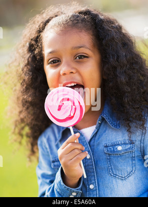 Mixed Race girl licking lollipop outdoors Banque D'Images