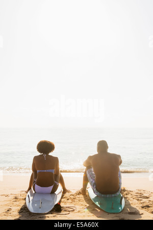 Couple sitting on surfboards on beach Banque D'Images