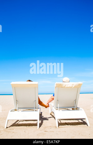 Couple holding hands in lounge chairs on beach Banque D'Images