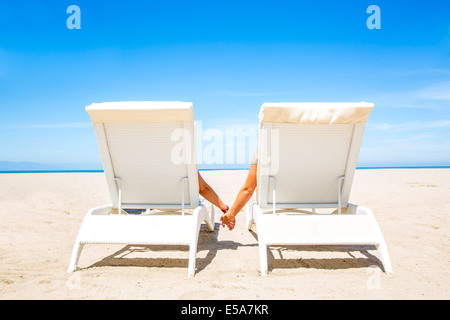 Couple holding hands in lounge chairs on beach Banque D'Images