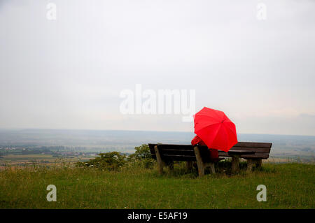 Homme avec parapluie rouge assis sur un banc, à un jour de pluie Banque D'Images