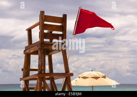 Lifeguard poster à une plage tropicale est abandonné en tant que drapeau rouge des vagues dans le vent. Banque D'Images