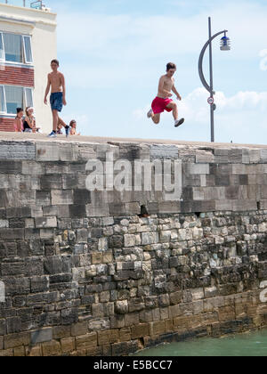 Un adolescent saute dans la mer depuis le haut de la chaleur dans les murs vieux Portsmouth. En dépit d'avertissement autour de la zone et l'augmentation des patrouilles de la pratique continue des jours chauds Banque D'Images