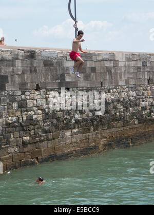 Un adolescent saute dans la mer depuis le haut de la chaleur dans les murs vieux Portsmouth. En dépit d'avertissement autour de la zone et l'augmentation des patrouilles de la pratique continue des jours chauds Banque D'Images