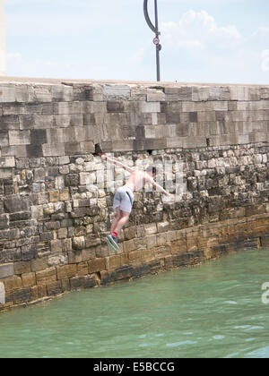 Un adolescent saute dans la mer depuis le haut de la chaleur dans les murs vieux Portsmouth. En dépit d'avertissement autour de la zone et l'augmentation des patrouilles de la pratique continue des jours chauds Banque D'Images