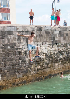 Un adolescent saute dans la mer depuis le haut de la chaleur dans les murs vieux Portsmouth. En dépit d'avertissement autour de la zone et l'augmentation des patrouilles de la pratique continue des jours chauds Banque D'Images