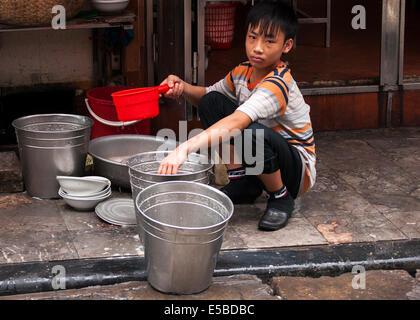 Le travail des enfants - triste à la jeune garçon de rincer les plaques dans les seaux en métal. Banque D'Images