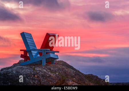 Le rouge et le bleu des chaises Adirondack sur rochers à McNeil Bay sur le détroit de Juan de Fuca au coucher du soleil-Victoria, Colombie-Britannique, Canada. Banque D'Images