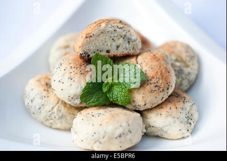 Cookies aux graines de pavot à la main avec une feuille de menthe placé sur le côté dans un bol blanc sur un fond blanc. Banque D'Images