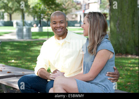 Un jeune couple interracial assis sur un banc sur une journée ensoleillée. Banque D'Images