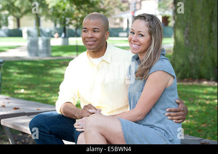 Un jeune couple interracial assis sur un banc sur une journée ensoleillée. Banque D'Images