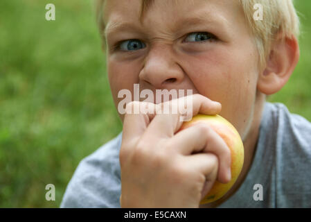 Portrait de l'enfant garçon blond Yeux bleu Eating Apple à l'extérieur, grin Banque D'Images