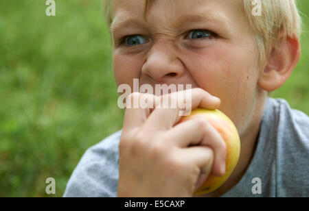 Portrait de l'enfant garçon blond Yeux bleu Eating Apple à l'extérieur, grin Banque D'Images