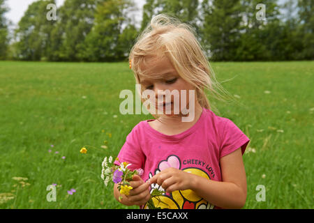 Petit enfant fille blonde sur le pré holding Flowers Banque D'Images