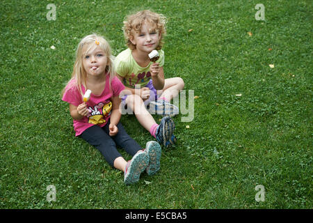 Enfants blondes eating ice cream cones assis sur la pelouse, l'heure d'été Banque D'Images