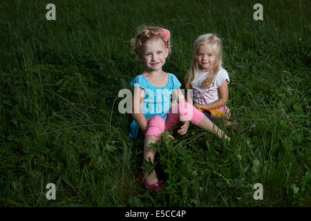 Portrait de deux jeunes filles blondes enfants sisters sitting in grassy field summertime Banque D'Images