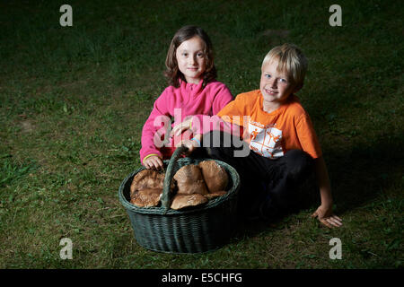 Enfants fille et garçon assis par panier plein de champignons sur pelouse verte à l'extérieur Banque D'Images