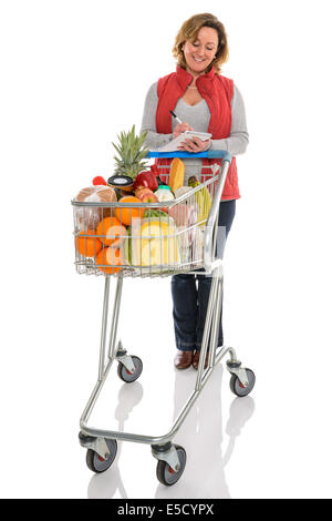 Une femme avec un chariot de supermarché rempli d'aliments frais contrôle de sa liste de courses, isolé sur un fond blanc. Banque D'Images