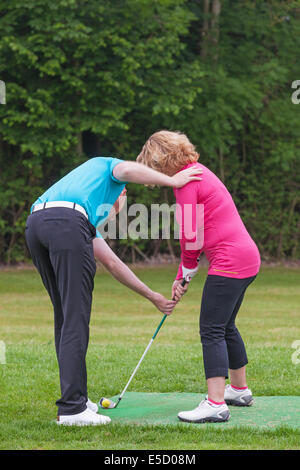 Un golfeur dame est enseigné à jouer au golf par un Pro sur une pratique d'entraînement. Banque D'Images