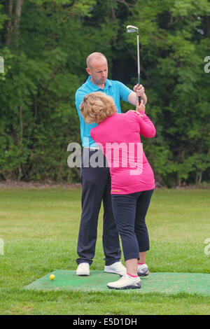 Un golfeur dame est enseigné à jouer au golf par un Pro sur une pratique d'entraînement. Banque D'Images