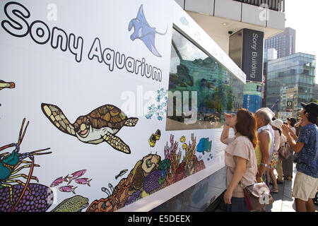 Tokyo, Japon - Les piétons voir les poissons d'Okinawa à l'intérieur du réservoir d'eau de 14 tonnes à l'entrée de l'immeuble Sony le 28 juillet 2014. La 47e 'Aquarium Sony' a été mis en place un aquarium en plein air de l'immeuble Sony d'événements, qui affiche des créatures d'Okinawa Churaumi Aquarium. Le réservoir recrée l'écologie des récifs de corail et la vie marine de l'îles Kerama. L'événement regroupe différentes activités pour les enfants et d'un film d'îles Kerama filmée en 4k. L'Aquarium dans le 47e Sony Tokyois ouvert du 25 juillet au 31 août. © Rodrigo Reyes Marin/AFLO/Alamy Live News Banque D'Images