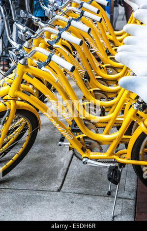 Une ligne d'un service de location de vélos jaunes sur l'affichage pour la transmettre à la foule les jours de marché à Broadway dans le centre-ville de Columbus, Géorgie, USA. Banque D'Images