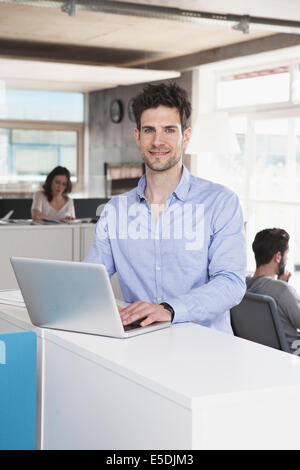 Portrait of smiling man with laptop debout dans l'open space office Banque D'Images