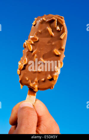 Jeune homme main tenant une glace au chocolat sur le ciel bleu Banque D'Images