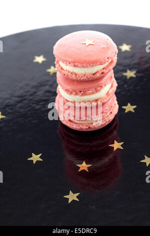 Trois macarons rose sur une surface brillante noire avec étoiles d'or Banque D'Images