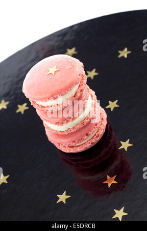 Trois macarons rose sur une surface brillante noire avec étoiles d'or Banque D'Images