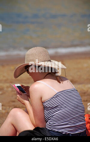 Femme à l'aide de téléphone mobile sur la plage de Worbarrow Bay, à l'île de Purbeck, Dorset en Juillet Banque D'Images