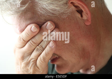 Man couvre ses yeux avec sa main dans la douleur ou le stress émotionnel. Banque D'Images