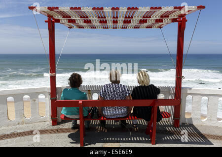 Trois femelles assis sur un banc à l'ombre regardant la mer Silverira, Portugal Banque D'Images