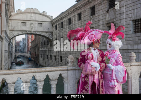 Dix-huitième siècle couple noble en rose sur le pont par le doge's Palace pendant le carnaval de Venise. Banque D'Images