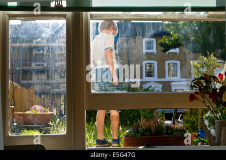 Boy standing in garden de maison vue à travers la vitre Banque D'Images