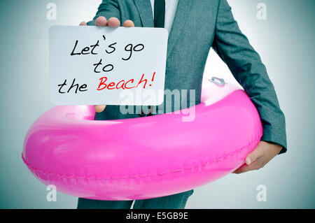 Businessman with a pink swim ring montrant une pancarte avec le texte allons à la plage écrit en c Banque D'Images