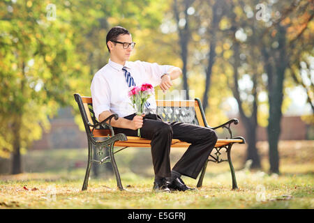 Jeune homme qui attendait son jour assis sur banc dans park Banque D'Images