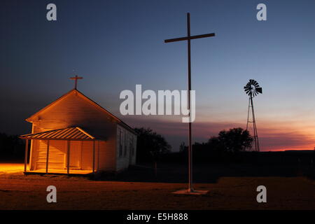 Une église est éclairée par une lumière comme le coucher du soleil s'efface derrière une croix et moulin à vent, au Texas, USA. Banque D'Images