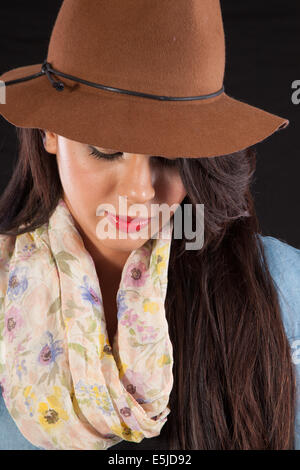 Jolie brunette aux cheveux longs femme en chapeau brun, debout avec une expression pensive mais plaidé Banque D'Images