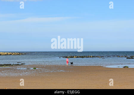 Femme entre chien sur Runswick Bay, North Yorkshire, Angleterre, Royaume-Uni. Banque D'Images