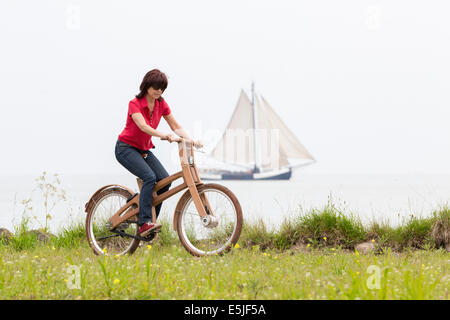 Pays-bas, Pingjum, Woman Riding the Bough Vélo. Le Dutch Design vélo en bois est une création de Jan Gunneweg. Bateau à voile Banque D'Images