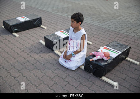 Berlin, Allemagne. 07 août, 2014. Un garçon palestinien dans une chemise avec taches rouges se trouve à côté de la taille des boîtes symbolisant enfant-cercueils à Neptunbrunnen à Berlin, Allemagne, 02 août 2014. Environ 500 personnes ont manifesté pour la paix en Palestine "' à Berlin d'après la police. Photo : Joerg Carstensen/dpa/Alamy Live News Banque D'Images